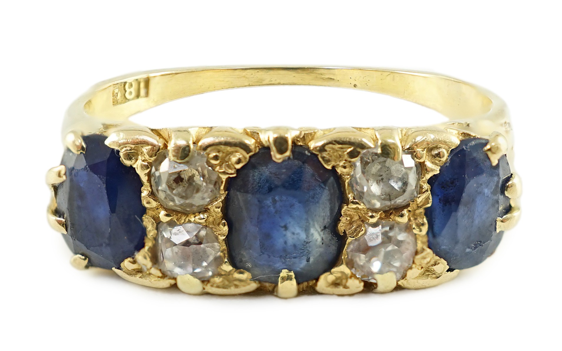 An early 20th century 18ct gold, three stone oval cut sapphire and four stone diamond spacer set half hoop ring